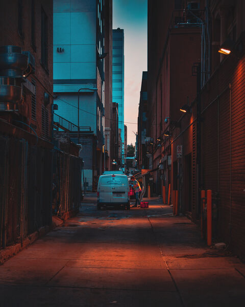 A white Royal Blue Grocery van stands in a narrow downtown alley at first light. A worker unloads beside its open side door, and lamps glow on the brick walls.